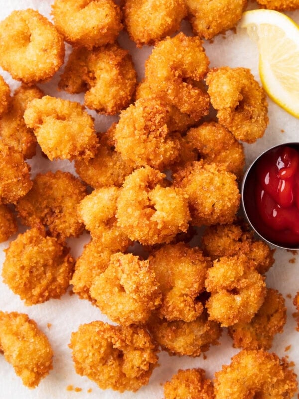 Lots of crunchy fried popcorn shrimp on a paper towel lined pan with lemon wedges and dipping sauce.