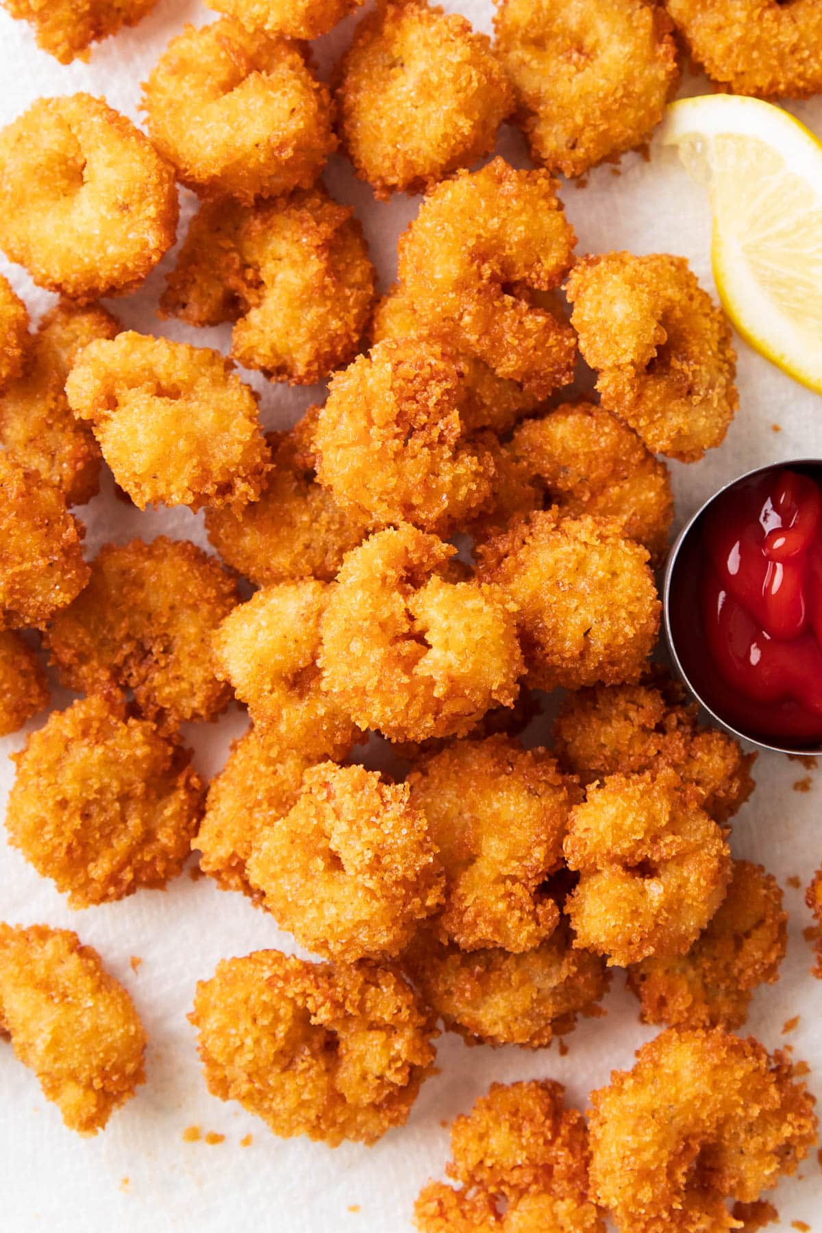 Lots of crunchy fried popcorn shrimp on a paper towel lined pan with lemon wedges and dipping sauce.