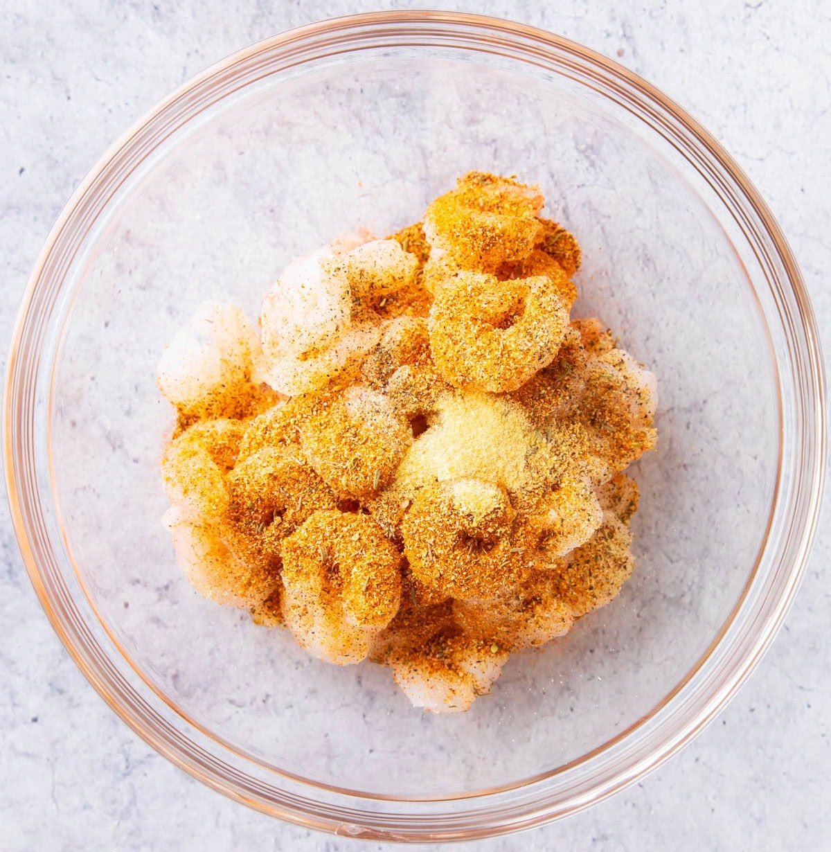 Seasoning on raw shrimp in a mixing bowl.