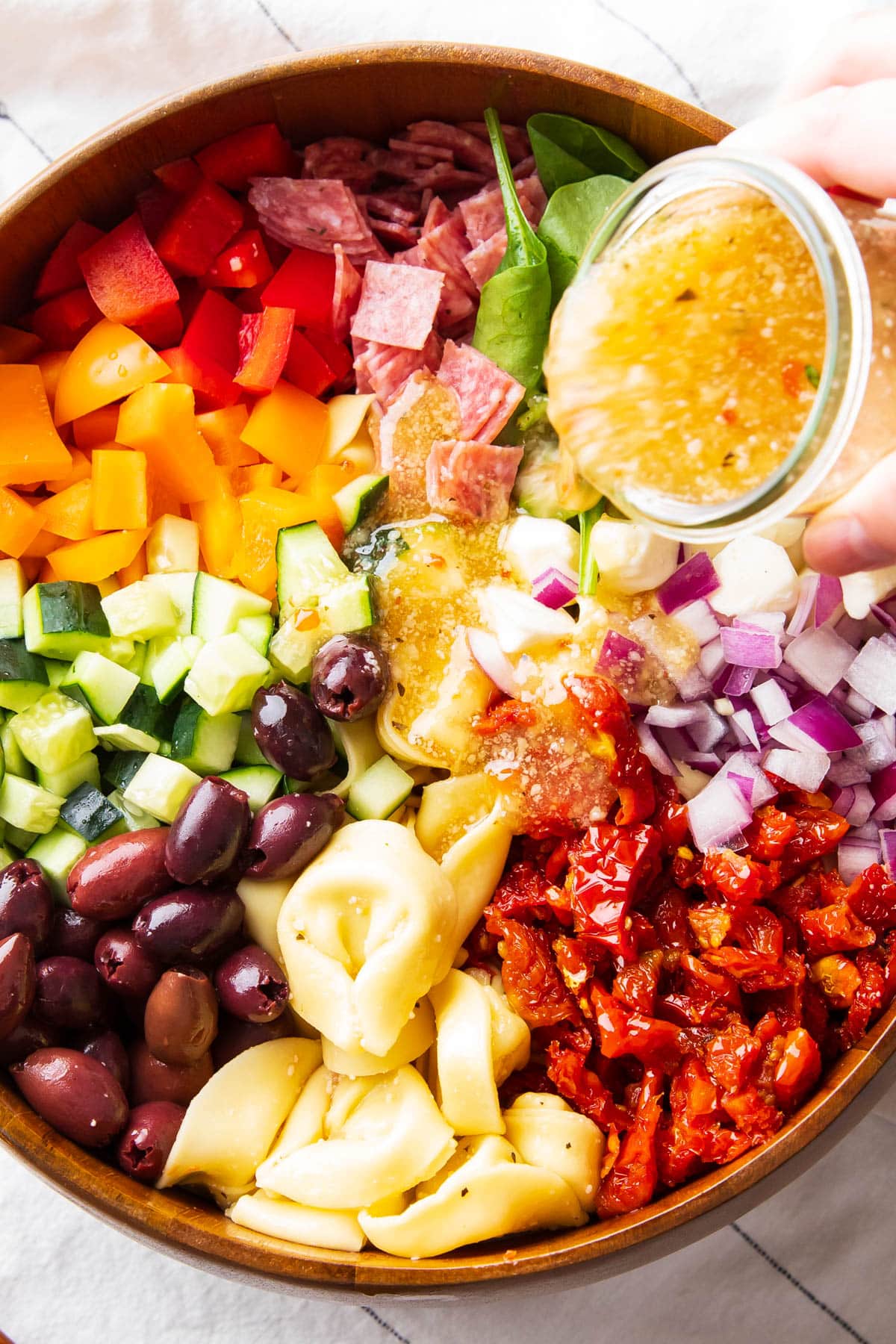 Someone pouring dressing over the pasta salad with tortellini ingredients.