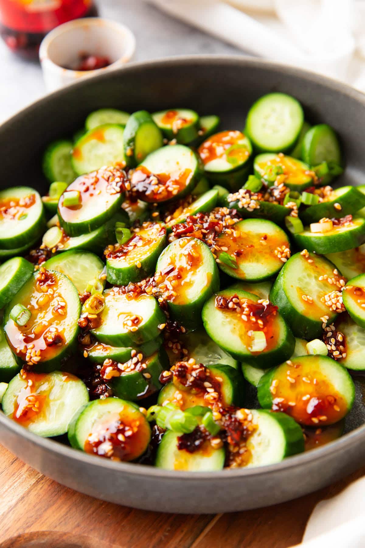 Asian cucumber salad served in a large rimmed dish topped with spicy dressing.
