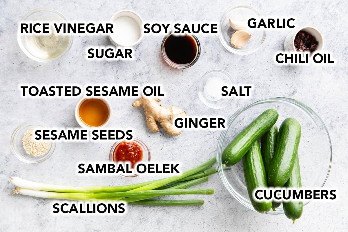 Asian cucumber salad ingredients with labels: cucumbers, rice vinegar, soy sauce, sugar, garlic, chili oil, ginger, sesame seeds, and scallions.
