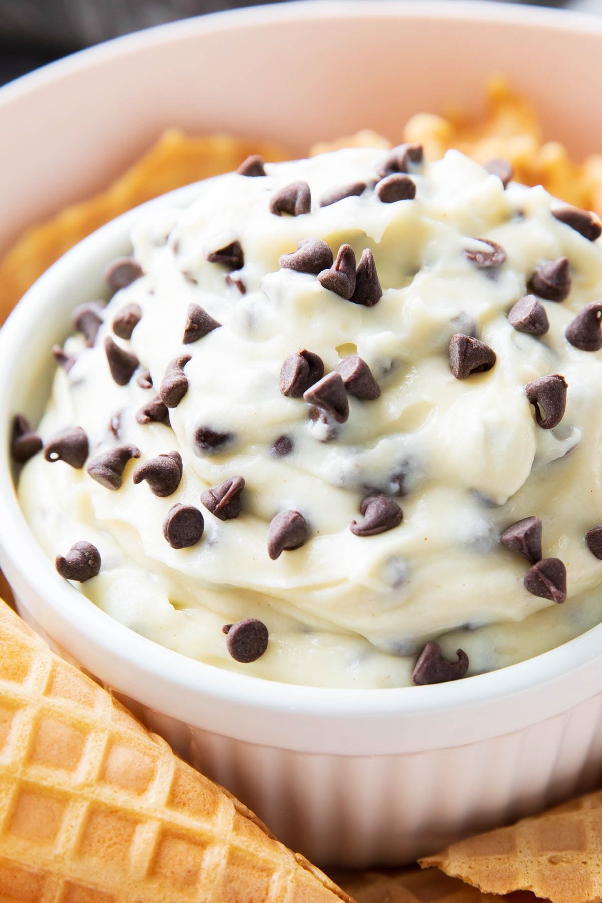 Close up of this cannoli dip recipe to show thick, smooth mascarpone-packed texture with lots of chocolate chips on top.