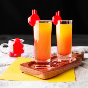 This pineapple upside down cake shot recipe includes grenadine and layers of pineapple juice and vodka on a serving tray with maraschino garnishes.