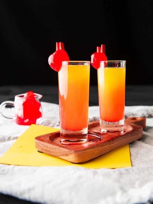 This pineapple upside down cake shot recipe includes grenadine and layers of pineapple juice and vodka on a serving tray with maraschino garnishes.