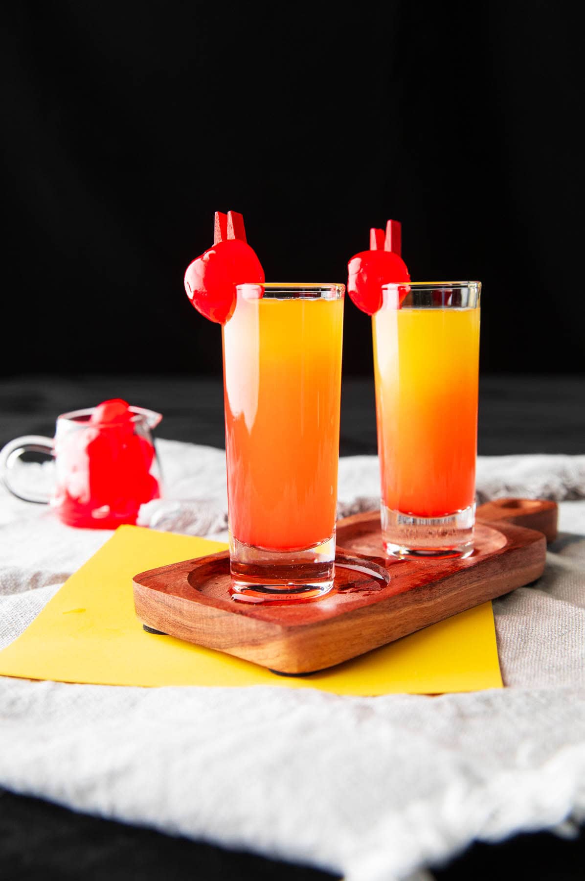 This pineapple upside down cake shot recipe includes grenadine and layers of pineapple juice and vodka on a serving tray with maraschino garnishes.