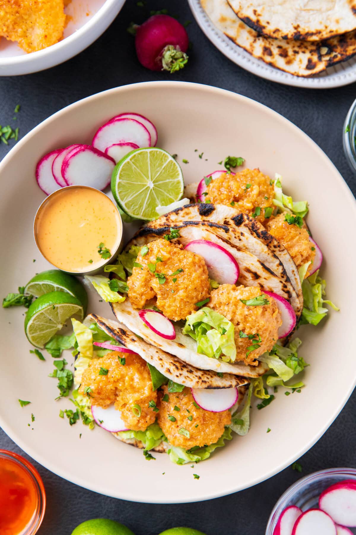 bang bang shrimp tacos recipe served on a plate with fresh lime wedges, extra bang bang sauce, cilantro, and more taco toppings
