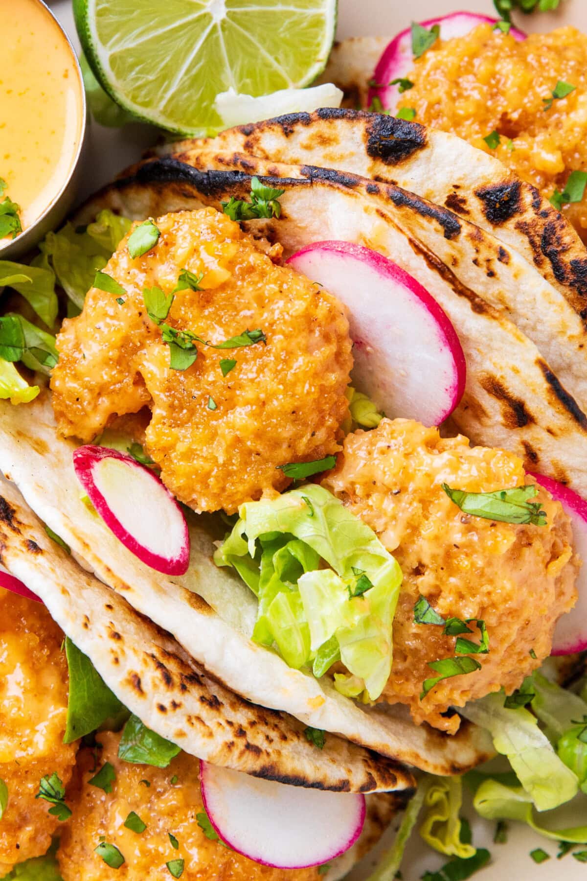 close up of bang bang tacos to show crispy shrimp coated in bang bang sauce with fresh lettuce in flame-grilled tortillas