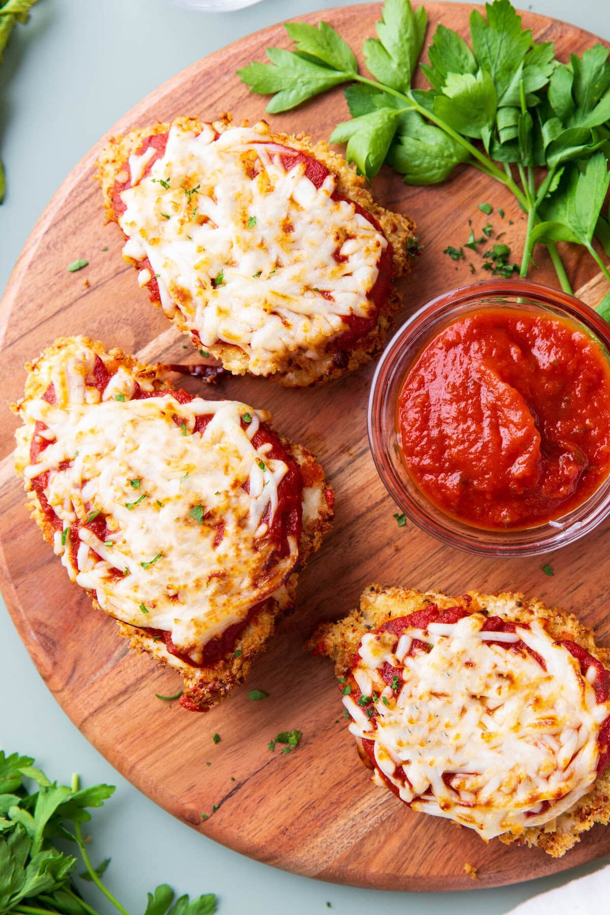 Platter of this air fryer chicken parmesan recipe with crispy breading served with bowl of marinara sauce and fresh parsley