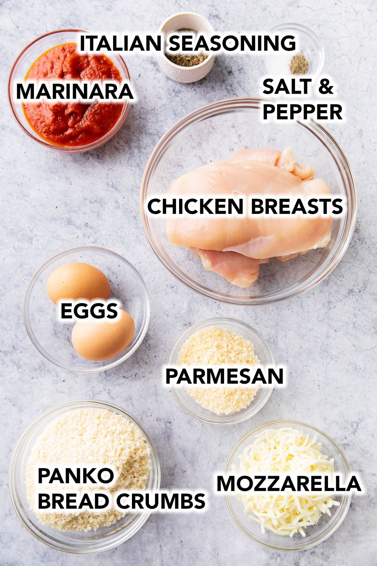 the ingredients for this air fryer chicken parmesan recipe measured in bowls including chicken breasts, marinara, eggs, Parmesan, mozzarella, panko bread crumbs, and seasonings.