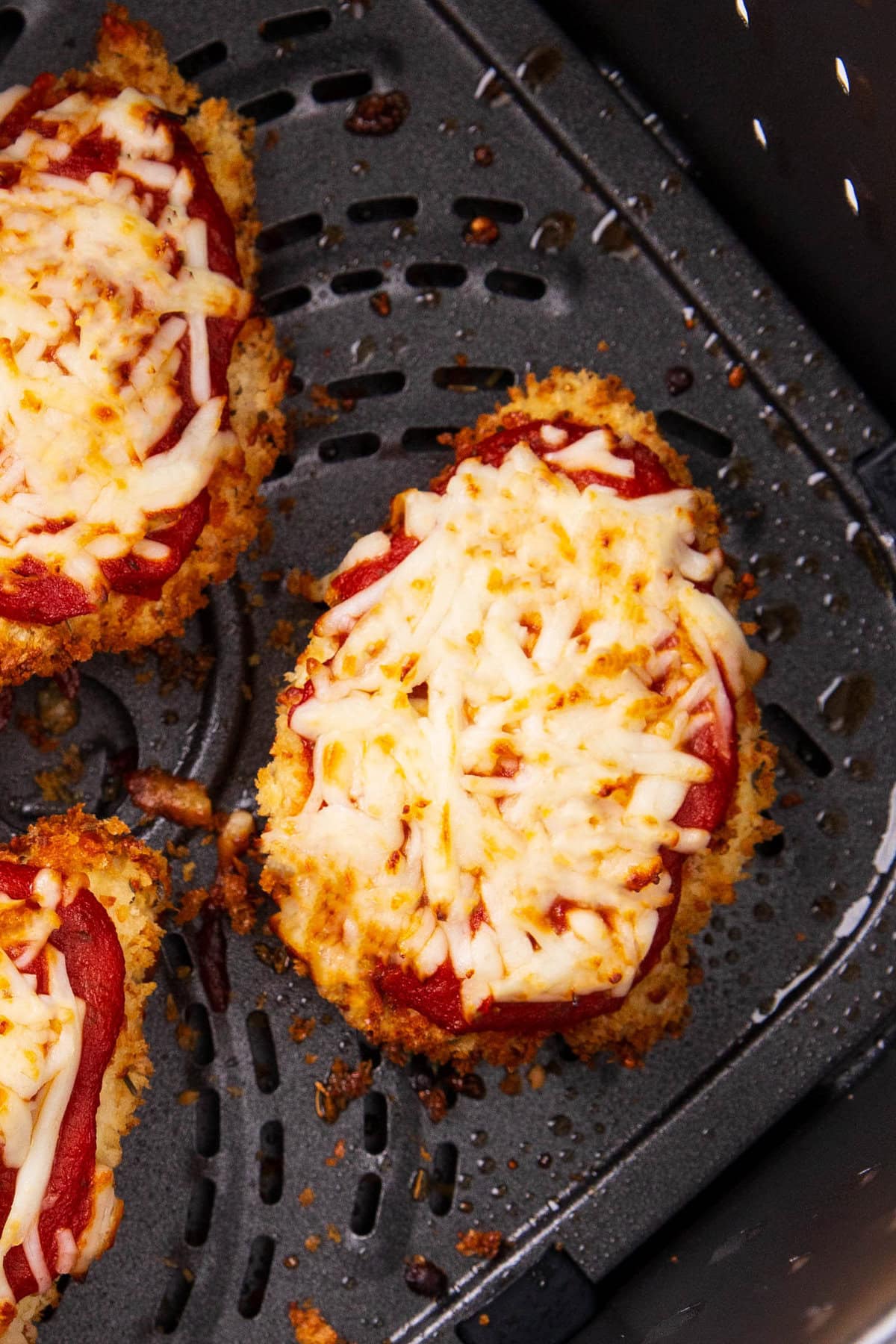 fully cooked air fryer chicken Parmesan in air fryer basket with melted cheese on top