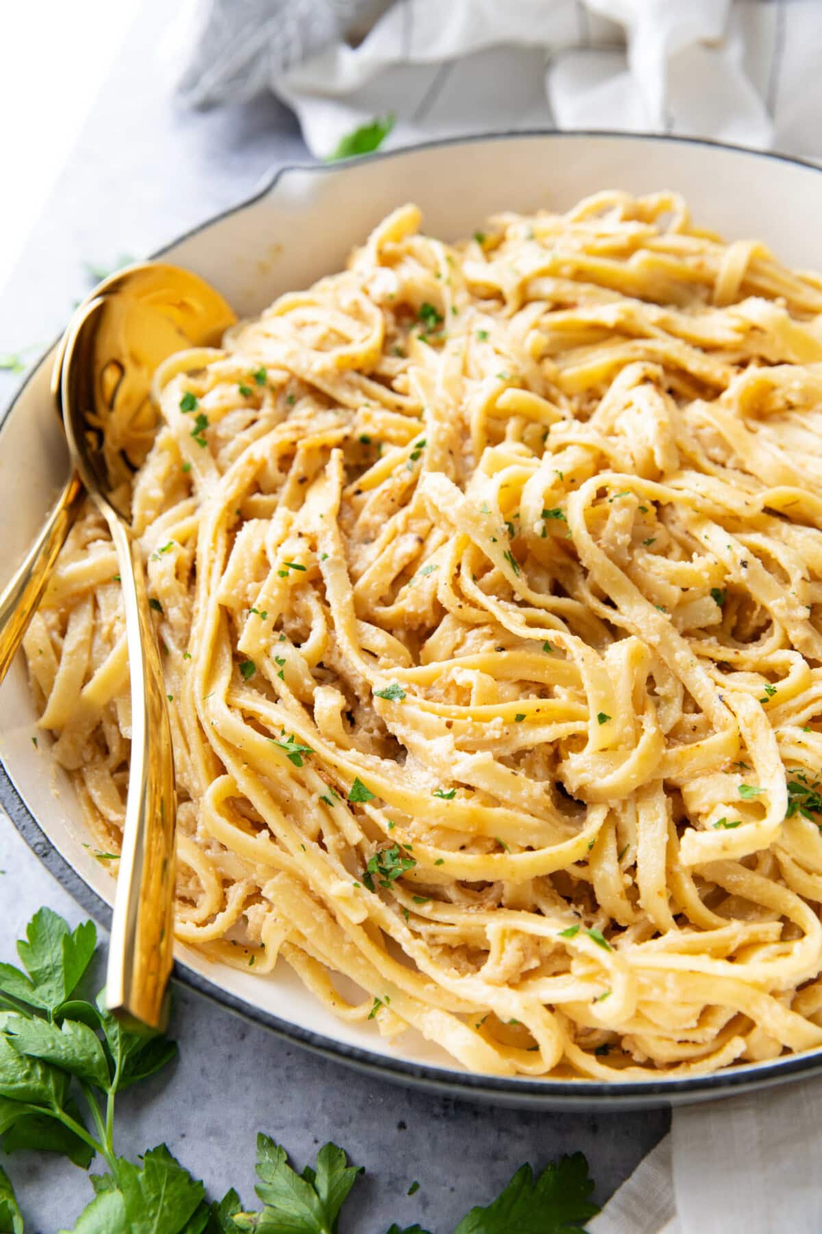 creamy Fettuccine Alfredo pasta served in a large pan with lots of sauce and gold tongs