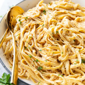 creamy Fettuccine Alfredo pasta served in a large pan with lots of sauce and gold tongs