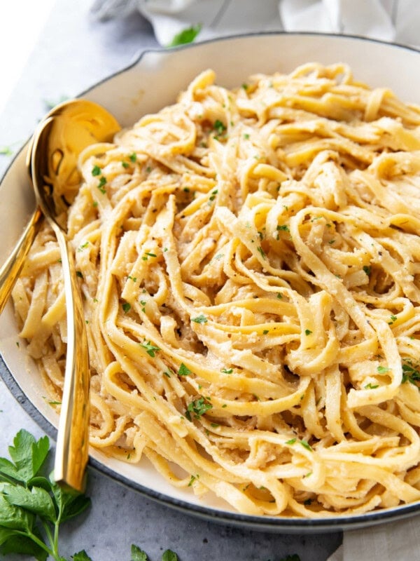 creamy Fettuccine Alfredo pasta served in a large pan with lots of sauce and gold tongs