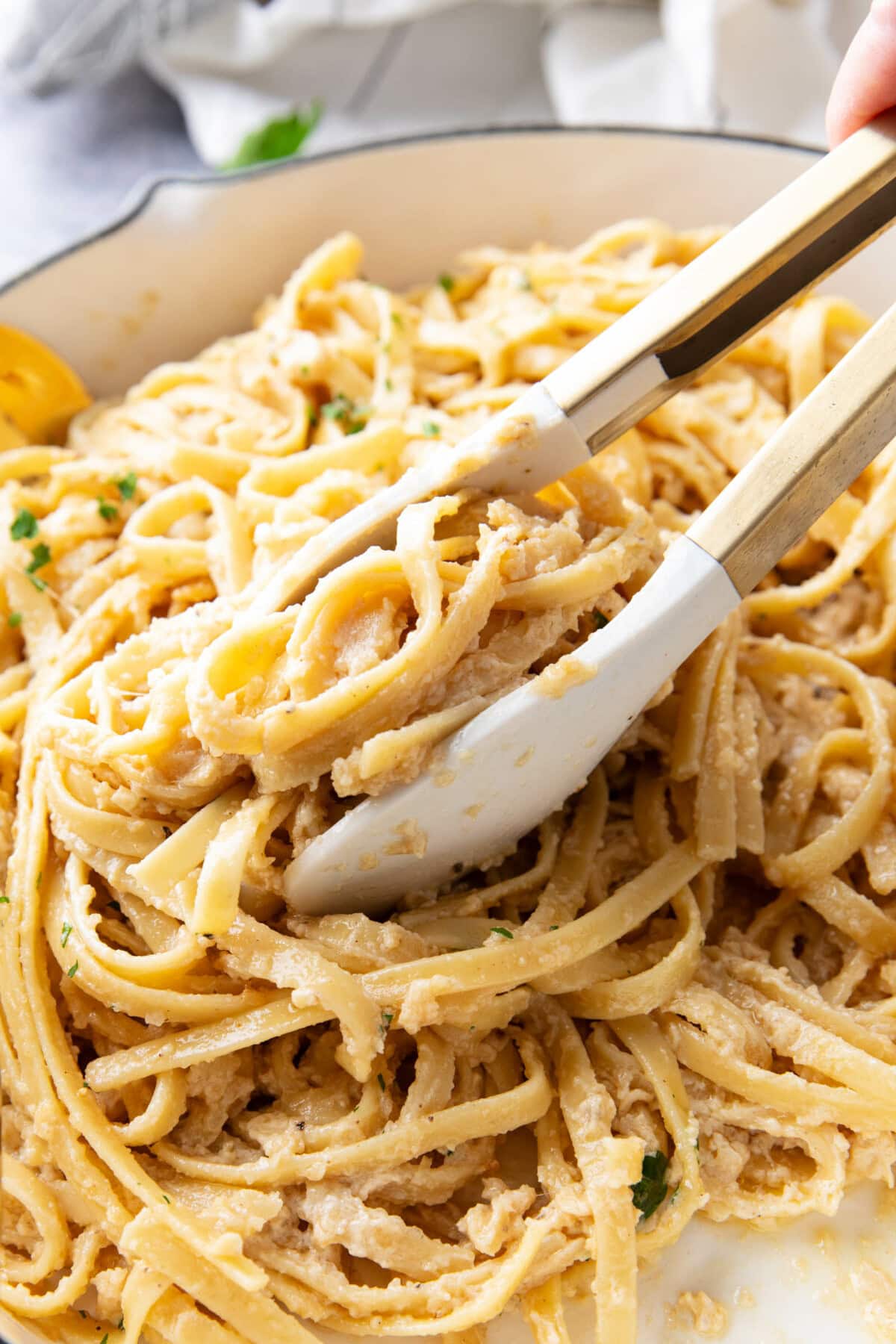 someone is grabbing a big scoop of this fettuccine Alfredo recipe with creamy sauce and chopped fresh parsley