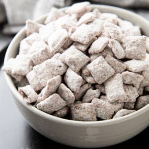 Bowl filled with Muddy Buddies coated in powdered sugar, chocolate and peanut butter