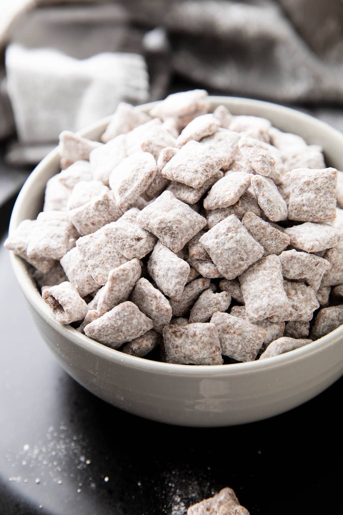 Bowl filled with Muddy Buddies coated in powdered sugar, chocolate and peanut butter