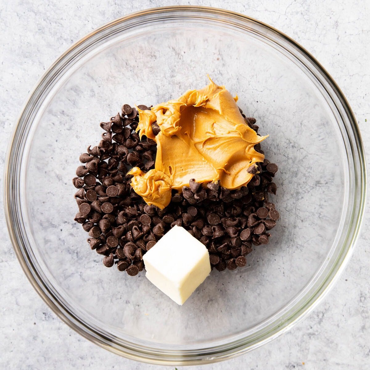 A photo showing How to Make Muddy Buddies - chocolate chips, peanut butter and butter in a mixing bowl
