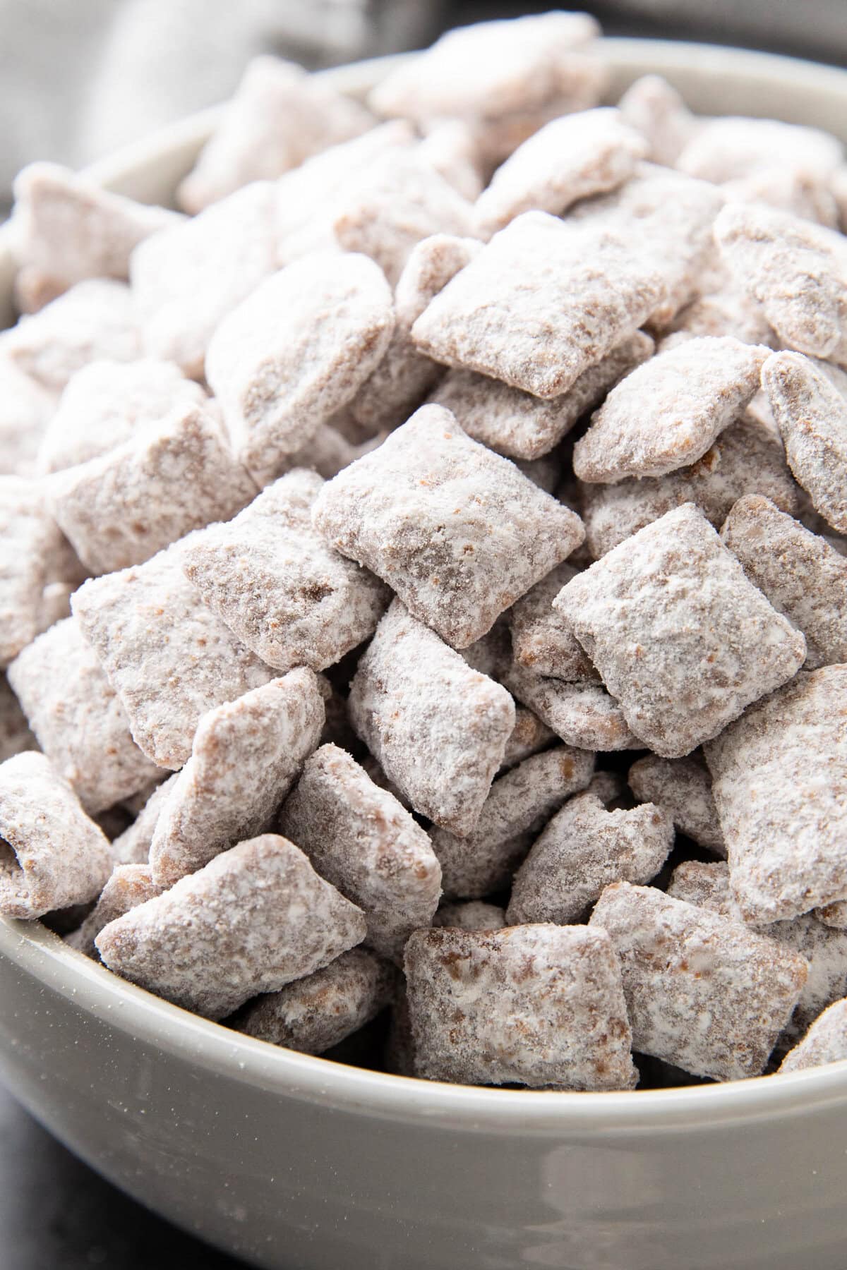 Close up of bowl of Muddy Buddies recipe showing individual pieces of Chex cereal coated in peanut butter and melted chocolate with powdered sugar