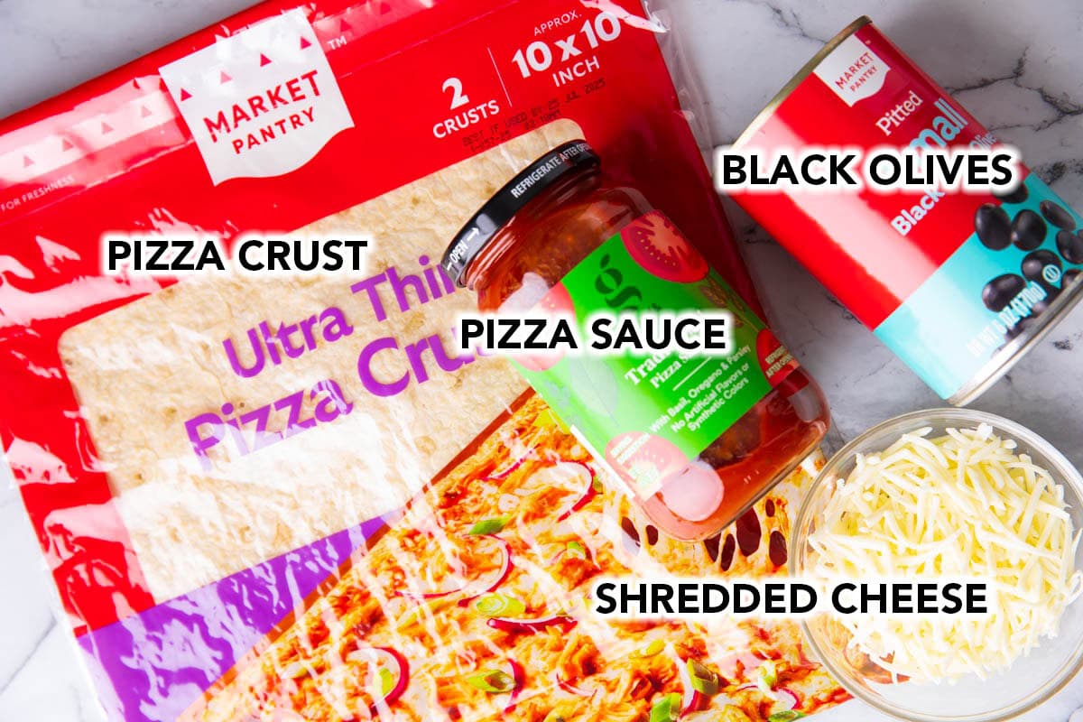 The ingredients for this Halloween pizza recipe laid out, including black olives, pizza crust, pizza sauce, and shredded mozzarella cheese