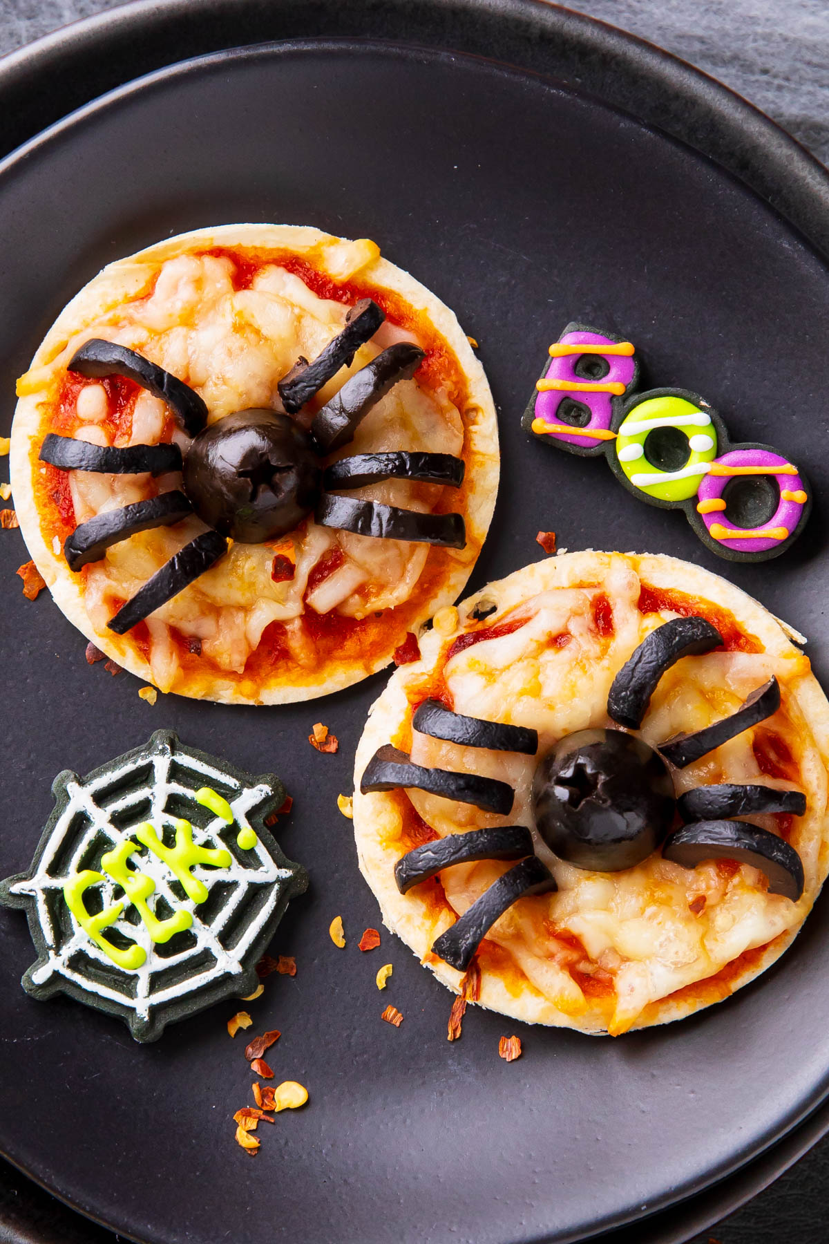 close up of cheesy Halloween pizzas topped with black olive spiders and a Boo party decoration