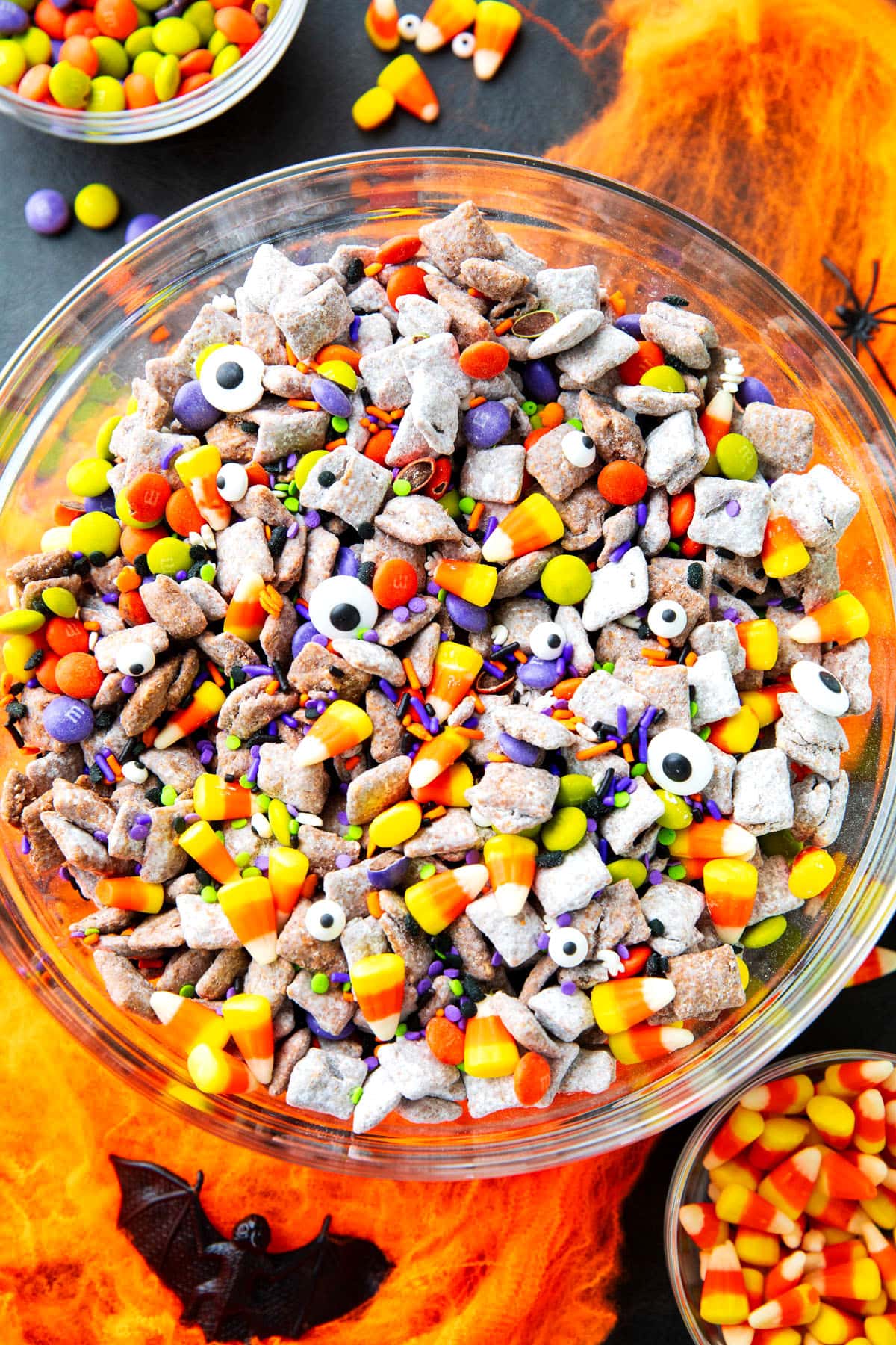 Halloween Puppy Chow served in a large mixing bowl filled with candy corn, googly eyes, and Halloween sprinkles.