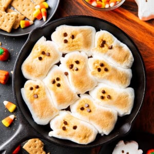 Halloween S'mores are topped with toasted ghost-shaped marshmallows serve on a Halloween party table with candy corn and graham crackers