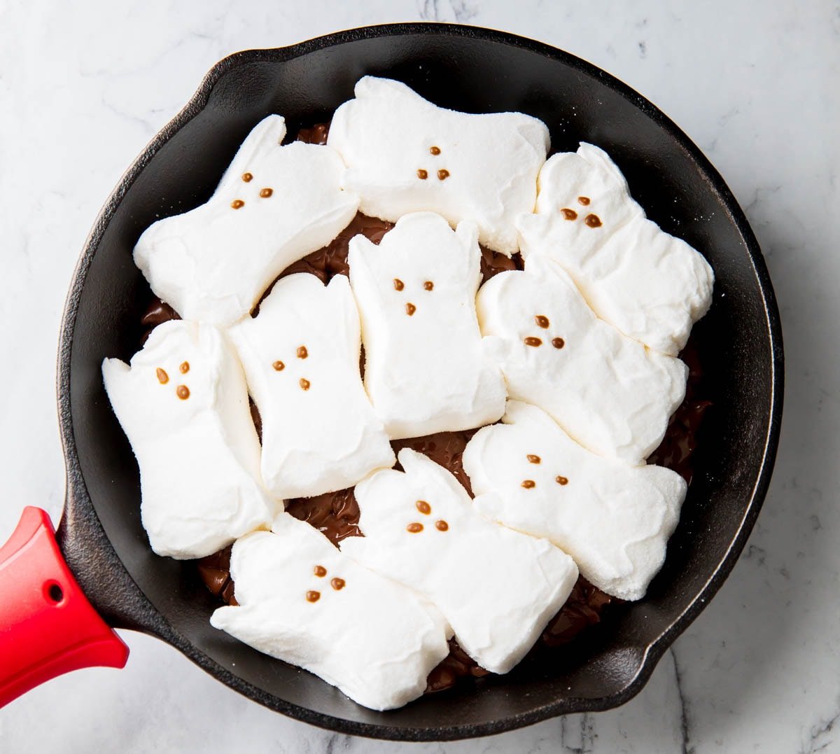 A photo showing how to make Ghost S'mores Dip - Ghost Peeps packed tightly on top of melted chocolate chips layer before baking.