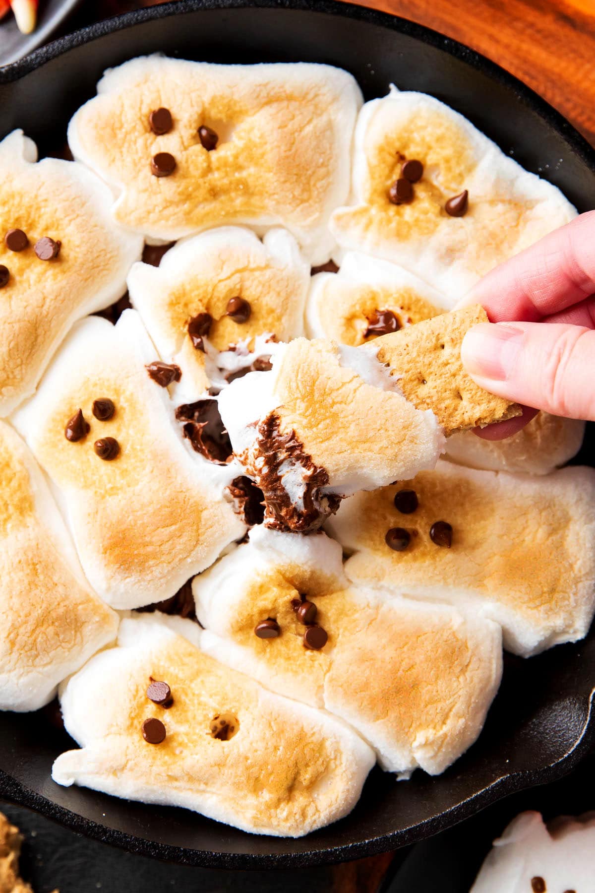 Someone dipping a graham cracker into this Halloween s'mores dip, with toasted marshmallows and chocolate on the cracker.