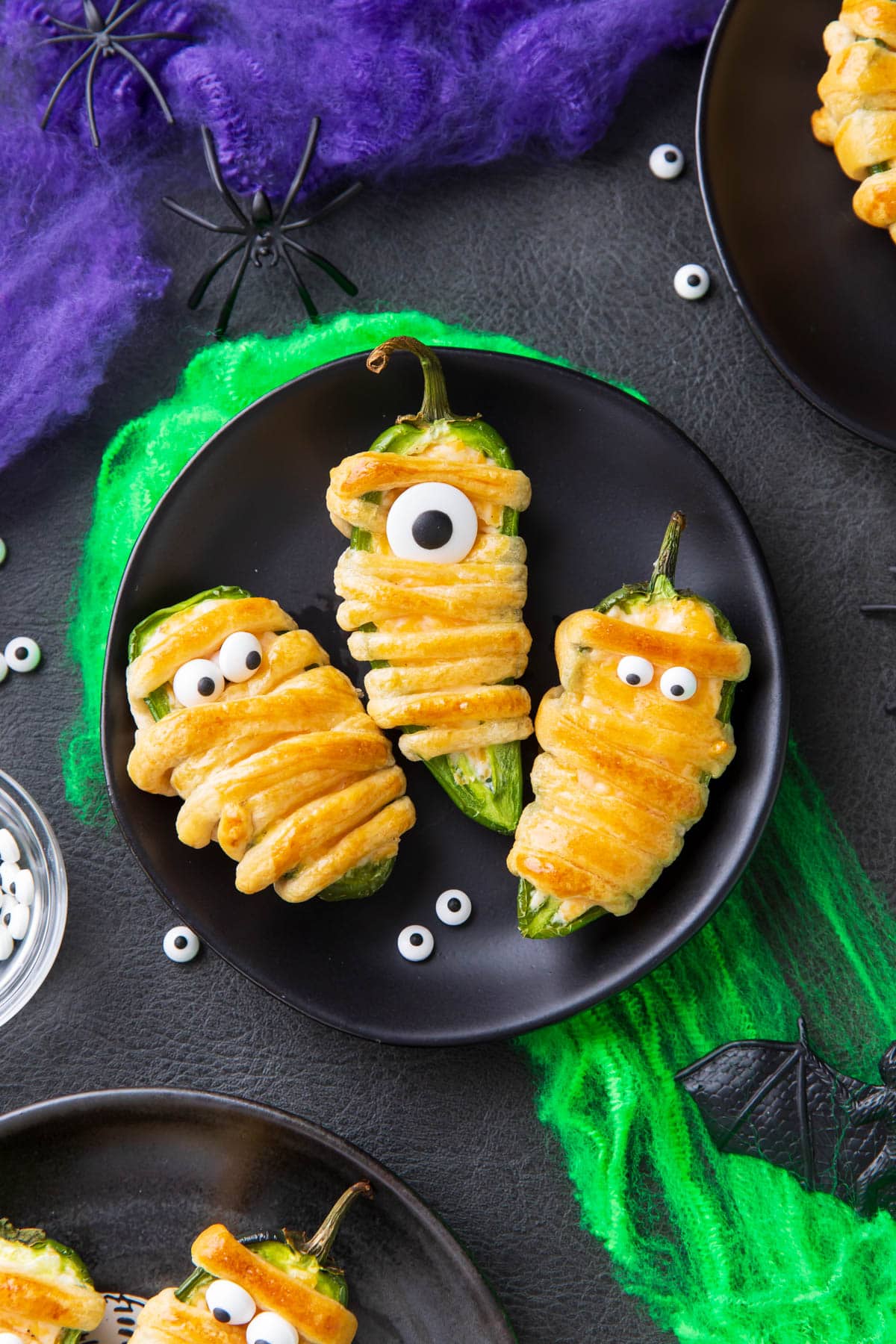 Mummy jalapeno poppers stuffed with cream cheese and wrapped in crescent roll dough is baked golden and served on a Halloween plate.