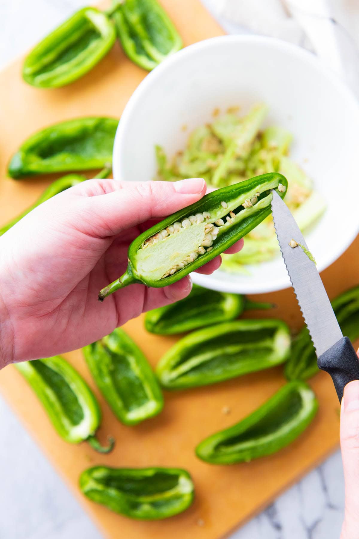 A photo showing How to Make Mummy Jalapeno Poppers - someone deseeding a jalapeno with a knife.