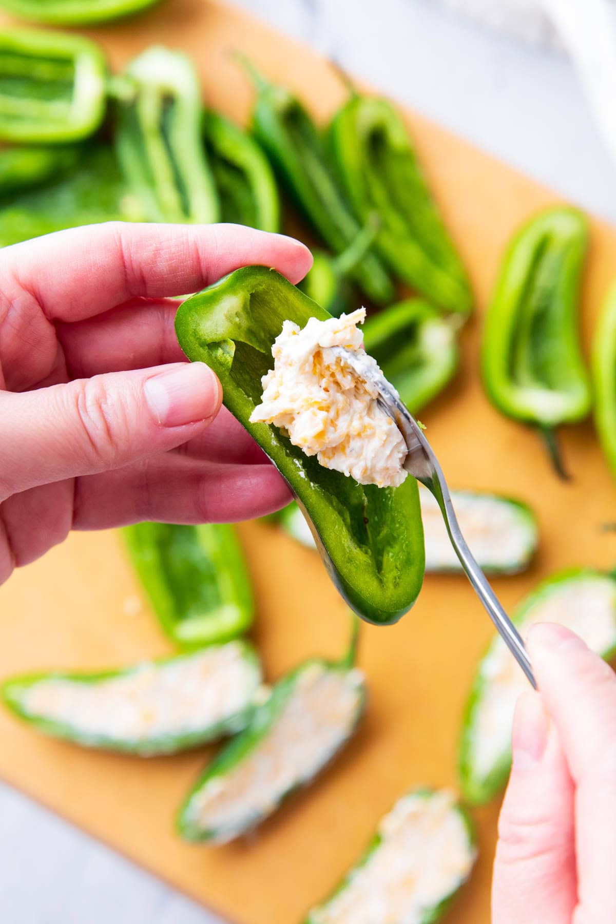 Someone adding cream cheese filling to a hollowed out jalapeno.