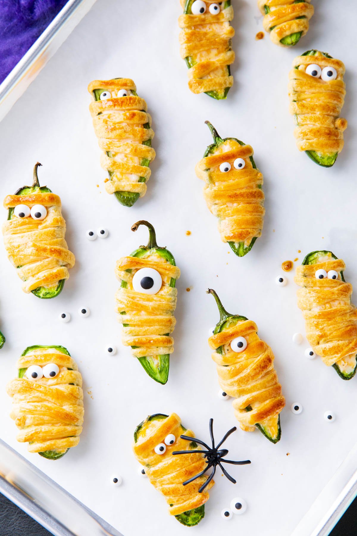 Googly eyes added onto this jalapeno popper mummies recipe spread out on a lined baking sheet.