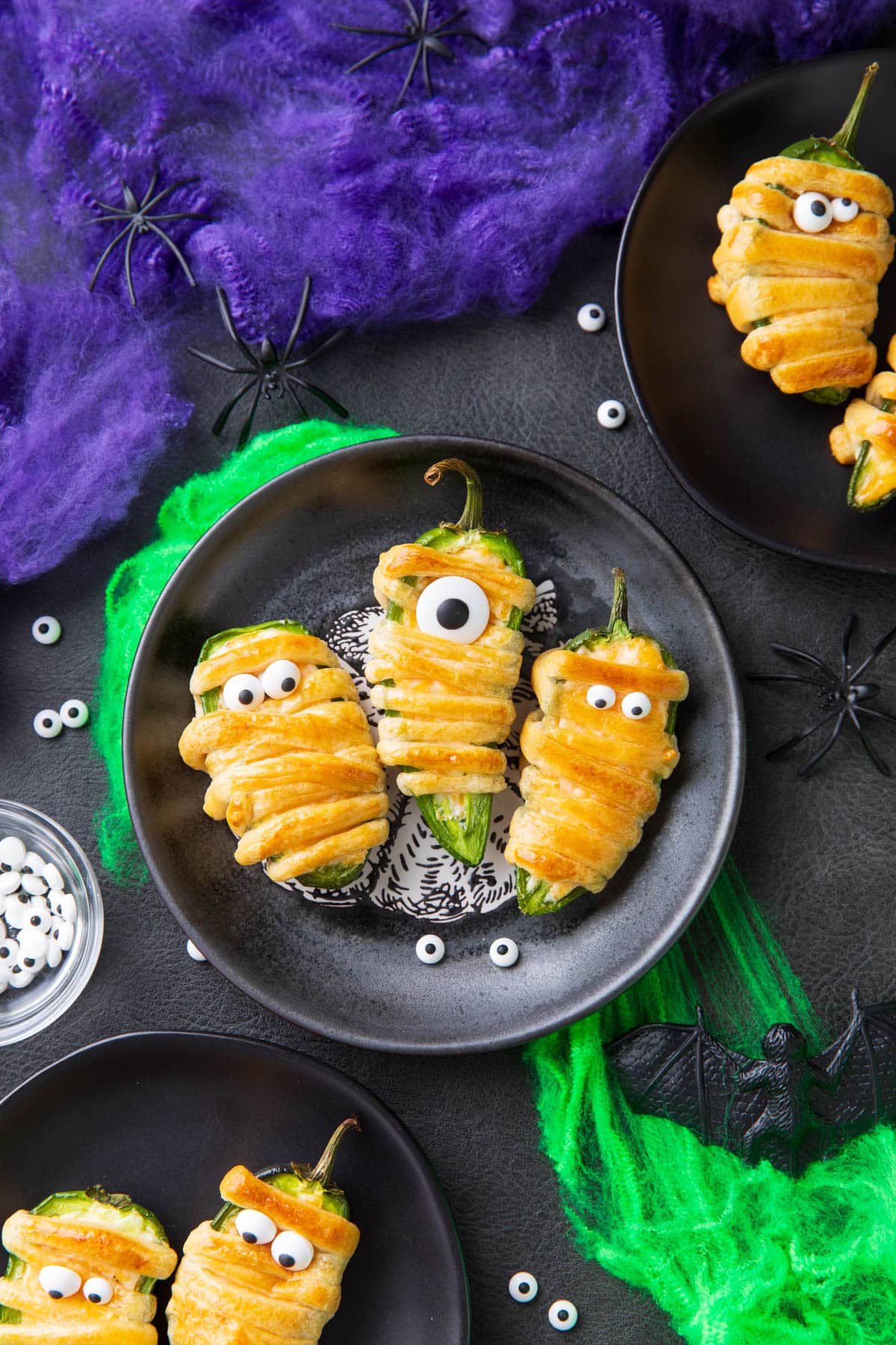 Jalapeno mummy poppers are a spooky appetizer served on a Halloween party table with bats, spiders, and festive decor.