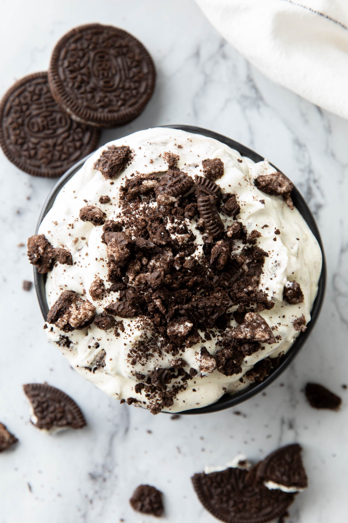 Oreo fluff with cream cheese served in a large appetizer dip bowl with Oreo cookies and crushed cookies nearby.