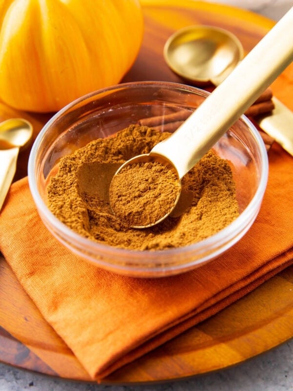 a measuring spoon scoops up pumpkin pie spice out of a spice bowl