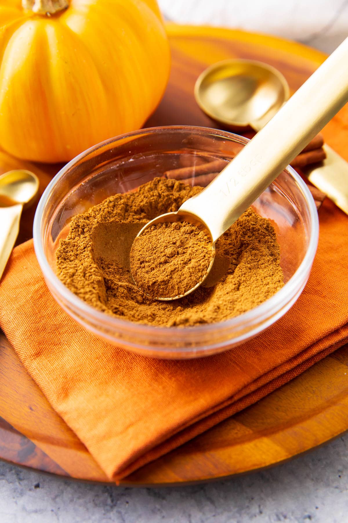 A measuring spoon scoops up pumpkin pie spice out of a spice bowl.
