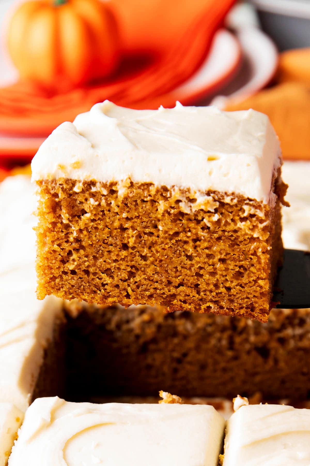 Someone grabbing a slice of this pumpkin spice cake with cream cheese frosting recipe on a cake spatula.