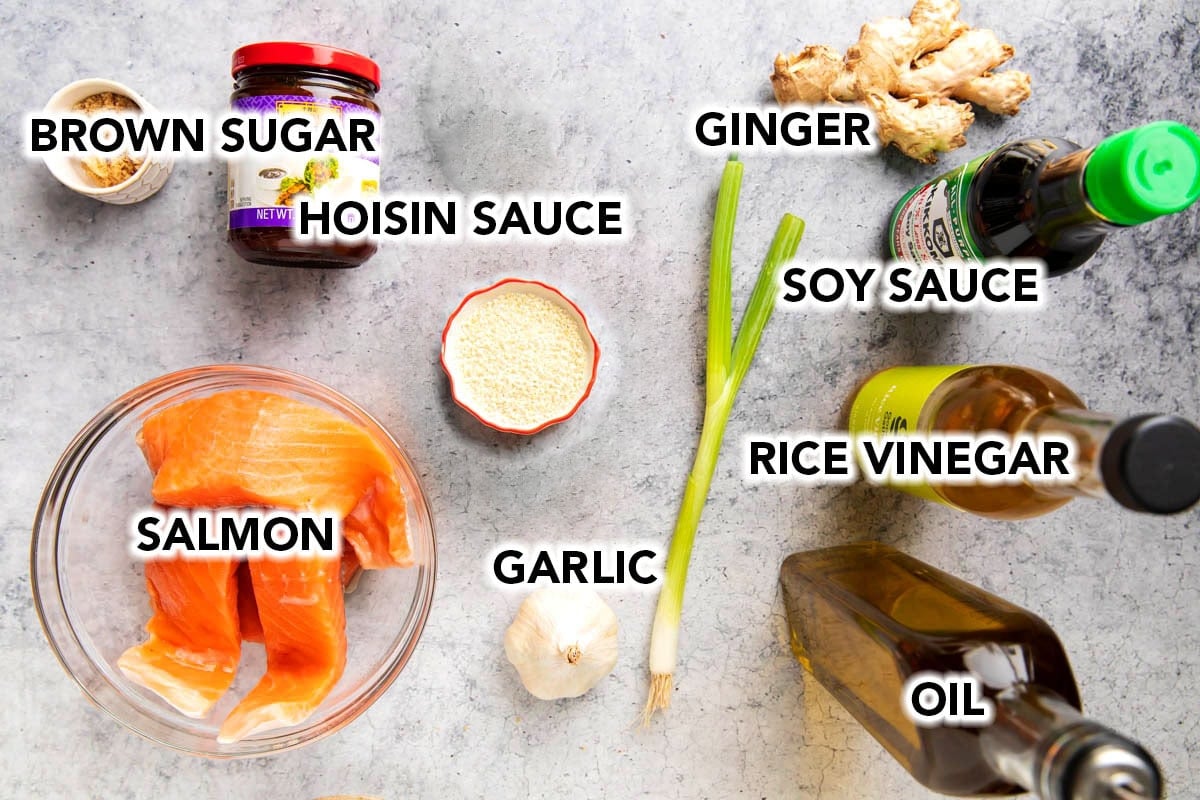 Asian baked salmon ingredients shown, including oil, soy sauce, garlic, hoisin sauce, rice vinegar, brown sugar, salmon fillets, green onions, and sesame seeds.
