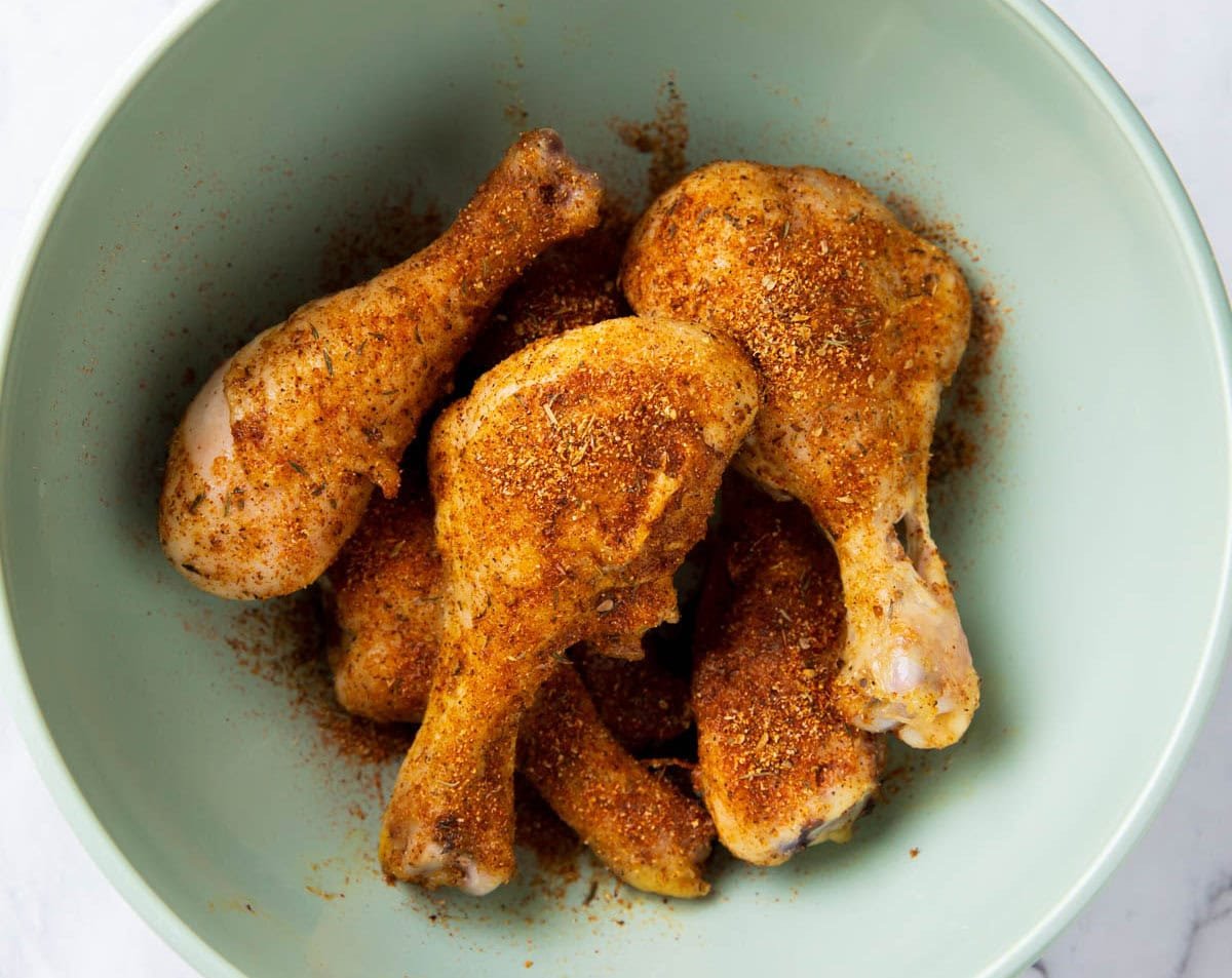 Oven baked chicken drumsticks are tossed in Cajun seasoning in a mixing bowl.