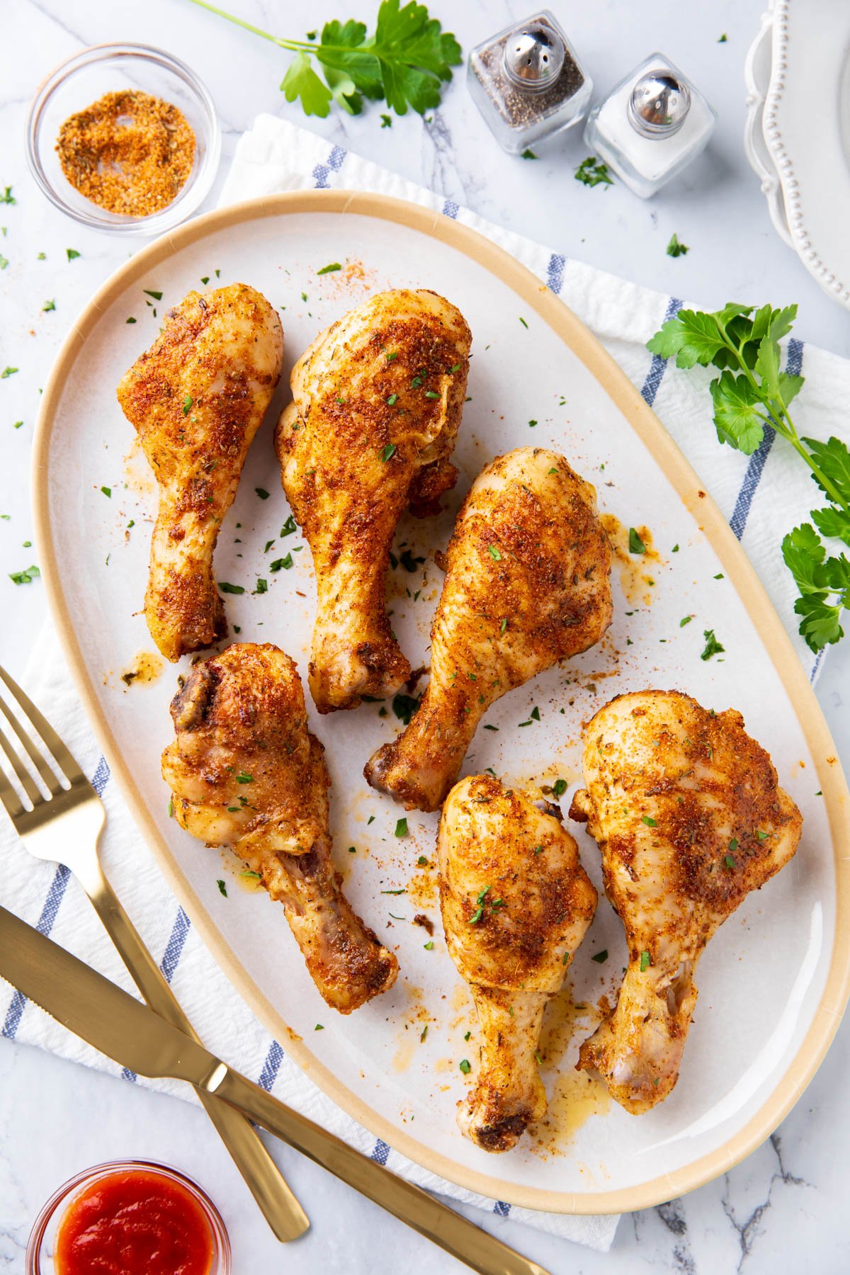 Cajun chicken drumsticks recipe is served on a platter with herbs and utensils for dinner.