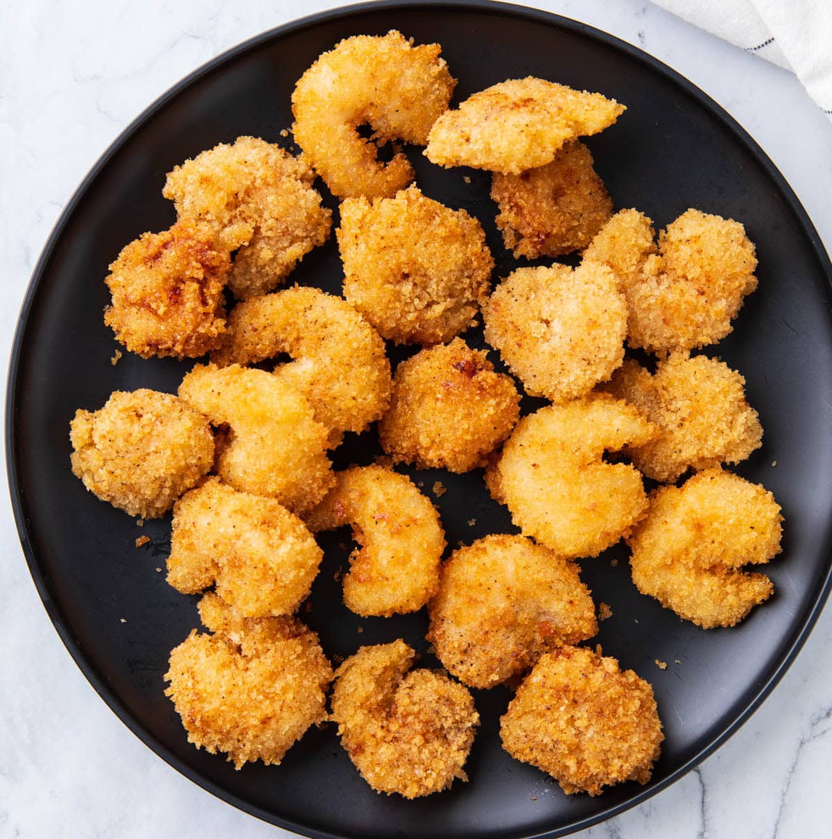 Crispy fried shrimp on a plate cooling before being coated in bang bang sauce.