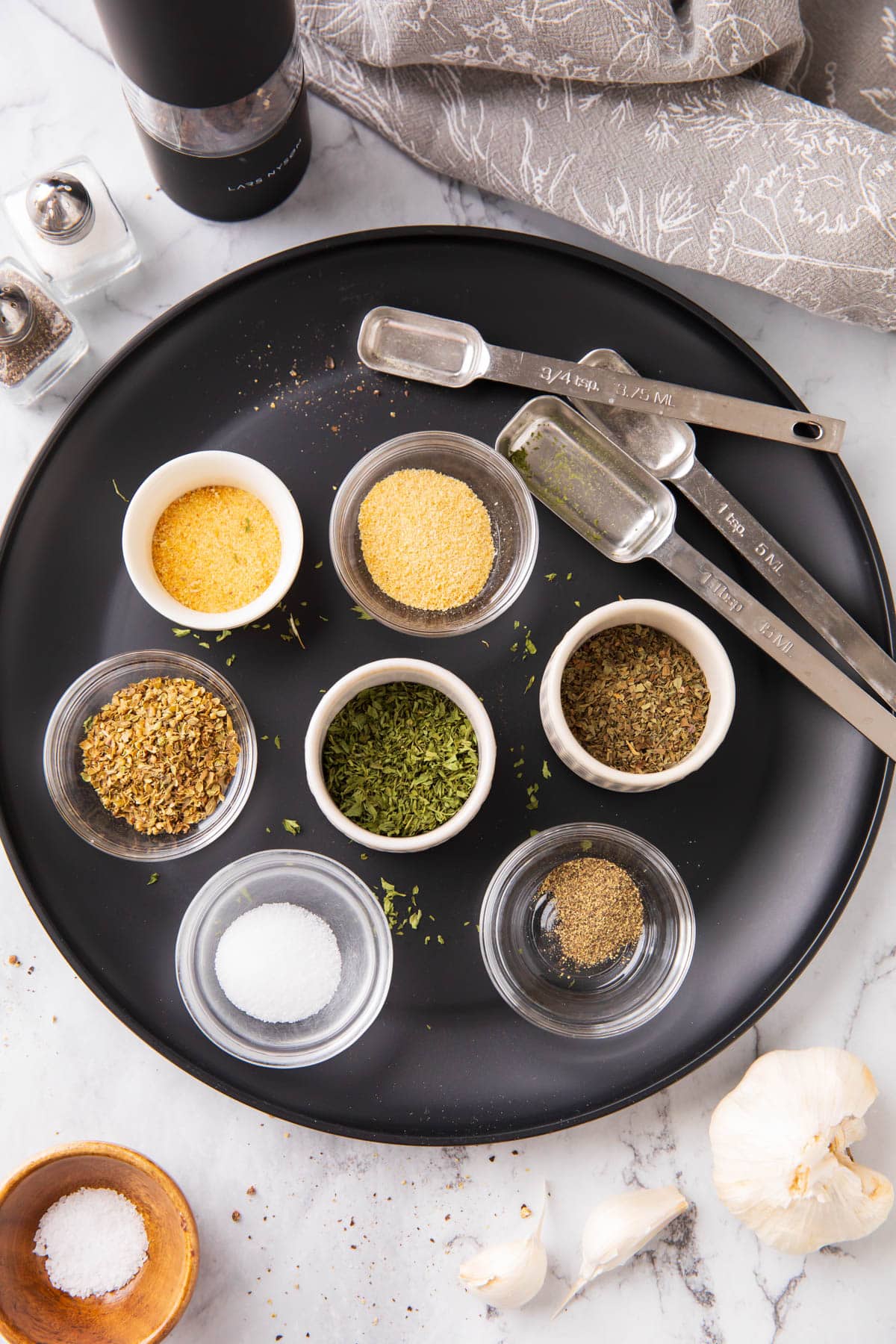 Individual spices measured into mise en place bowls to make garlic and herb seasoning.
