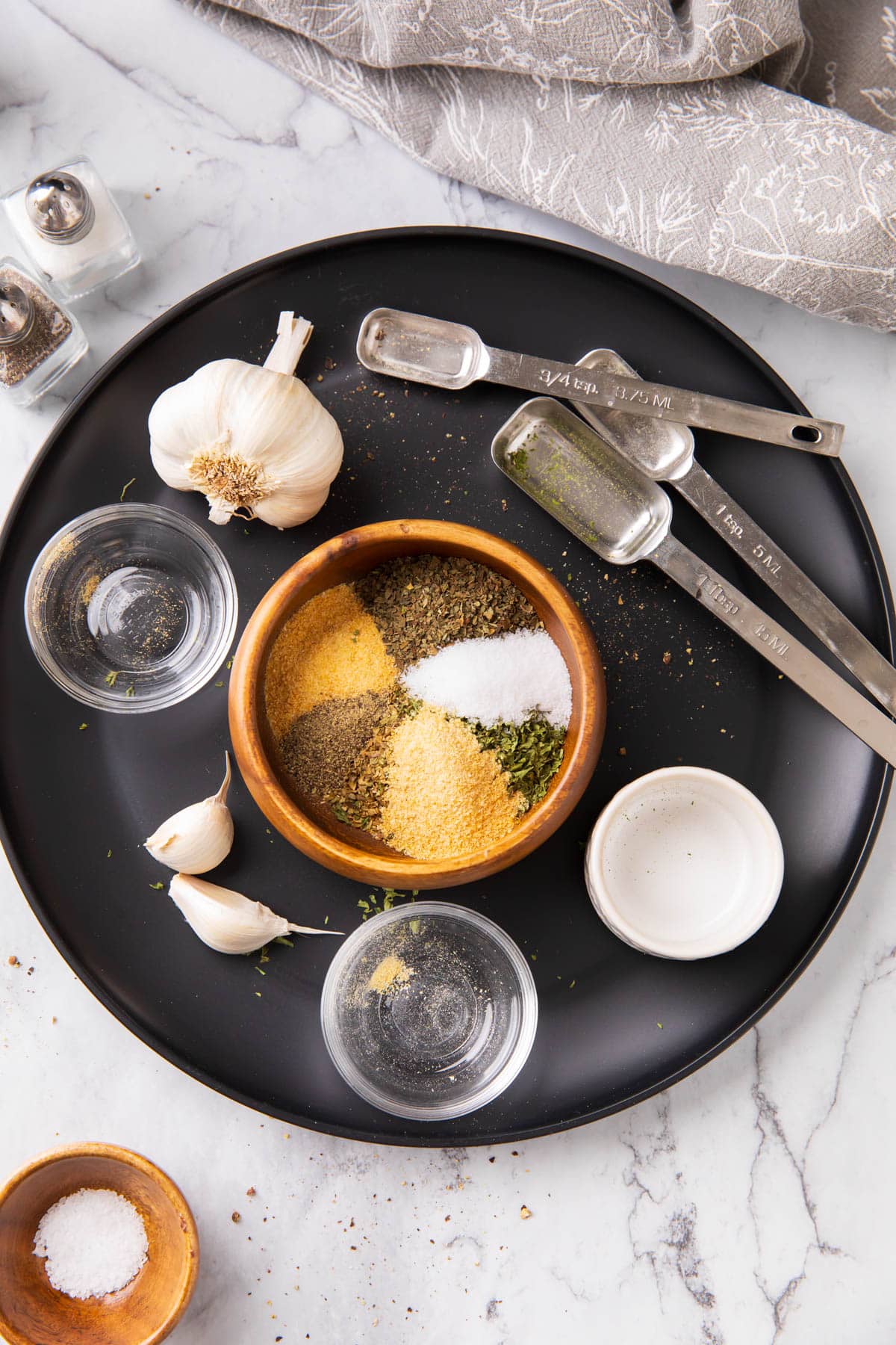Measuring spoons and bowls with the spices combined to make garlic and herb seasoning.