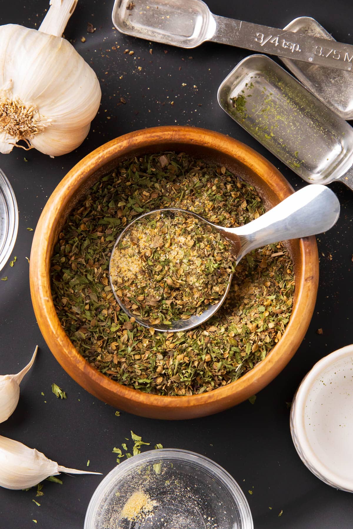 Overhead photo of this garlic and herb seasoning recipe in a bowl with a serving spoon and fresh garlic nearby.