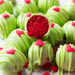 sliced in half Grinch Oreo Balls with bright red centers atop a pile of more Oreo Grinch Balls