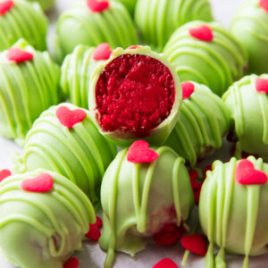 sliced in half Grinch Oreo Balls with bright red centers atop a pile of more Oreo Grinch Balls