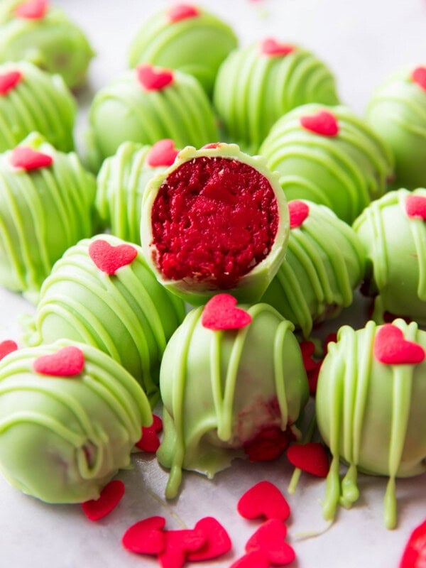 sliced in half Grinch Oreo Balls with bright red centers atop a pile of more Oreo Grinch Balls