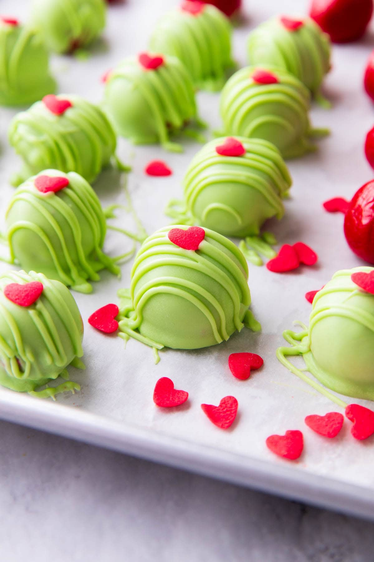 angled photo of thie Grinch Oreo Balls recipe with lots of green drizzle and hearts is a candy inspired by The Grinch Movie.