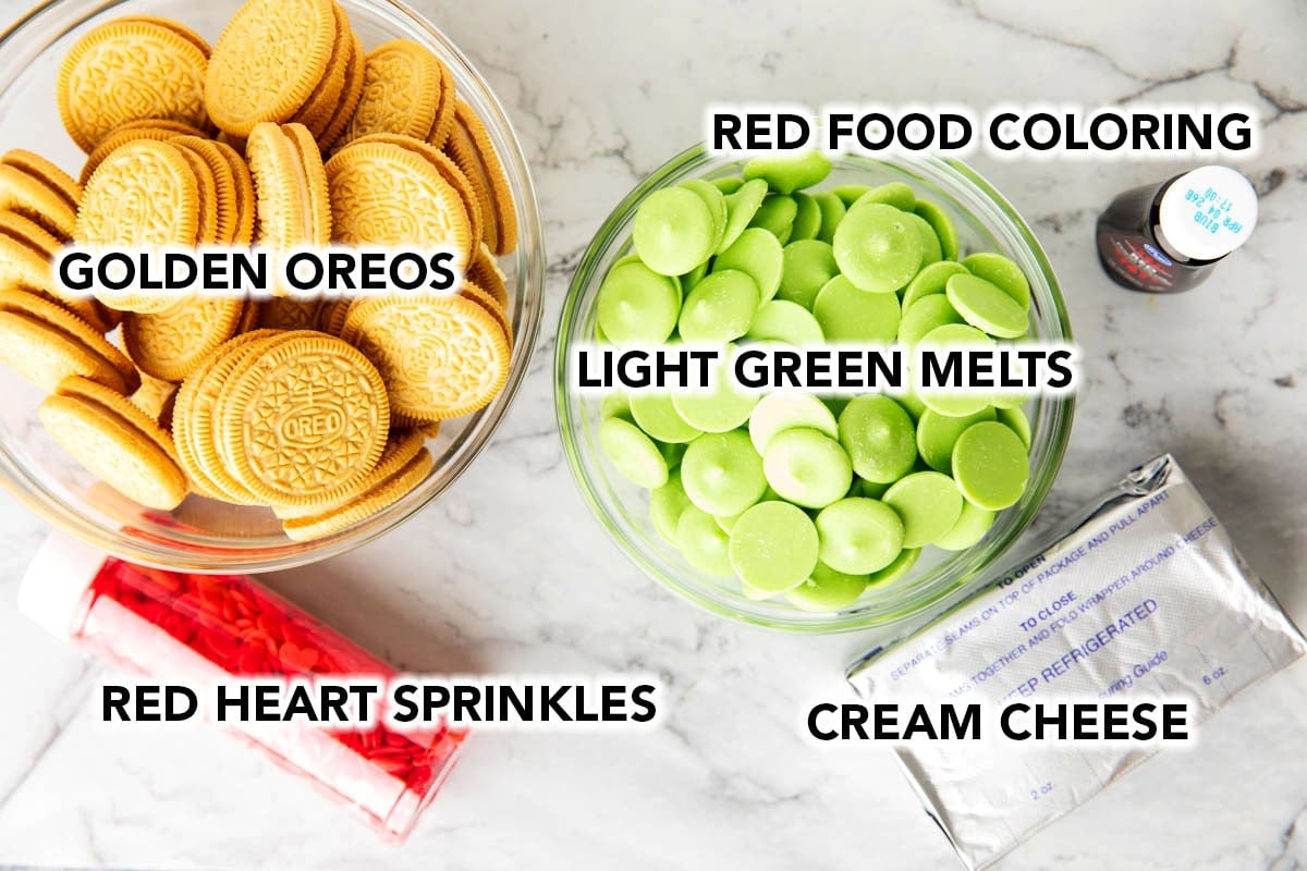 Grinch Oreo Balls ingredients measured into holiday bowls including golden oreos, light green candy melts, red heart sprinkles, cream cheese, and red food coloring.